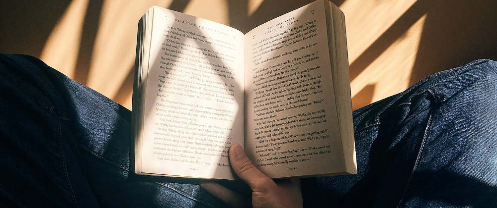 Person reading a novel in their lap under warm sunlight, wearing jeans — peaceful reading moment with natural light and shadows.
